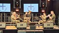 Ein Blechbläserquartett sitzt auf der Bühne und begleitet musikalisch den Gottesdienst.