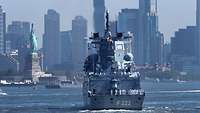 A gray warship in front of a city skyline with skyscrapers.