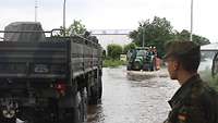 Ein Soldat steht auf einer überfluteten Straße. Ein Bundeswehr-Lkw fährt vor ihm durchs Wasser.