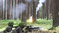 Soldaten liegen mit Waffen in einer Grube im Wald, im Hintergrund leuchtet es.