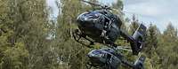 Zwei Hubschrauber fliegen dicht hintereinander. Ein Soldat schaut aus der Seitentür.
