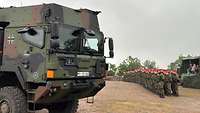 Ein Lastkraftwagen steht auf einen Platz, neben dem Fahrzeug stehen Soldaten in Formation.