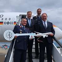 Zwei Soldaten und zwei Zivilisten stehen mit Schlüssel und Modellflugzeug auf einer Flugzeugtreppe 