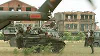 Ein Waffenträger Wiesel neben weiteren Gefechtsfahrzeugen wird von einem Soldaten eingewiesen
