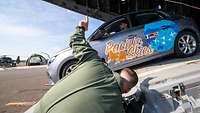 Ein kleines Auto mit dem Schriftzug "Pacific Skies" steht auf einer Laderampe.