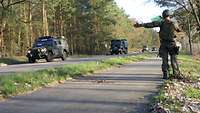 Ein Soldat gibt mit ausgestrecktem Arm und grüner Flagge Militärfahrzeuge auf einer Straße Zeichen