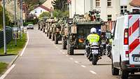 Mehrere Militärfahrzeug fahren in einer Kolonne auf einer Straße durch eine Stadt