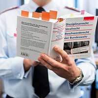 Ein Soldat hält ein Buch in der Hand, unter anderem zum Thema Disziplinarrecht 