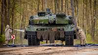 Ein Kampfpanzer Leopard 2 A7V wird von zwei Soldaten in ABC-Schutzkleidung dekontaminiert