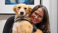 Eine Frau lächelt gemeinsam mit einem Hund in die Kamera.