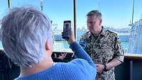 Eine Frau fotografiert an Deck eines Schiffs einen Soldaten mit einem Handy.