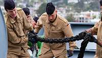 Soldaten halten auf Deck eines Schiffs ein dickes schwarzes Seil.