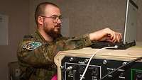 Ein Soldat steht an einem Laptop und einer IT-Plattform.