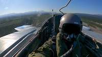 Ein Pilot sitzt im Cockpit während eines Flugs über einer Landschaft.