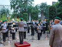 Militärmusik Viele Musikerinnen und Musiker in Uniform spielen auf ihren Instrumenten, vorn der Dirigent