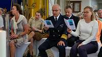 Mehrere Menschen sitzen an Deck eines Schiffes und singen