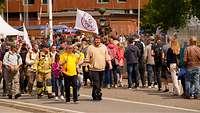 Zahlreiche Personen marschieren hintereinander durch ein militärisches Gelände