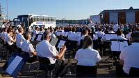 Ein Musikchor spielt vor einem Publikum unter freiem Himmel