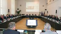 Mitglieder des Wehrmedizinischen Beirates sitzen in Sitzungssaal des Verteidigungsministeriumss.