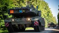 Mehrere gepanzerte Fahrzeuge fahren auf einer geteerten Straße durch den Wald