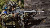 Zwei Soldaten im Gefechtsanzug stehen an einer Häuserecke im Wald