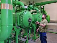 Pumpstation Ein Handwerker steht vor raumgroßen grünen stählernen Rohren und Pumpengehäusen und erklärt diese