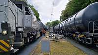 Rangieren Eine Güterzuglok sowie mehrere Kesselwagen stehen in einem Entladebahnhof auf Parallelgleisen.
