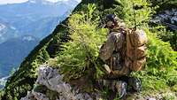 Ein Soldat mit Rucksack kniet im Gebirge und plant mit Hilfe einer Karte die Luftunterstützung.