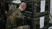 Ein Soldat arbeitet an Server-Einheiten, die in olivgrünen Transportboxen installiert sind