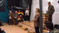 Zwei Frauen und drei Soldaten präsentieren etwas vor Publikum