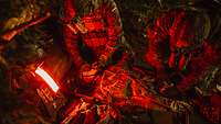 Soldaten behandeln eine Simulationspuppe bei Nacht. Ein portabler Lichtteppich leuchtet rot.