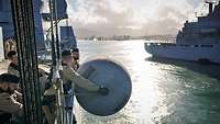 Marinesoldaten in sandfarbener Arbeitsuniform holen ein großes graues zylindrisches Objekt an Deck