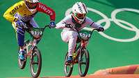 Zwei BMX-Radfahrer in Rennanzug und Helm und mit Startnummer am Lenker in voller Fahrt