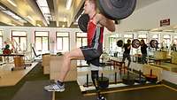 Ein Sportler mit aufgestelltem linkem Bein und Beinprothese rechts beim Training mit der Langhantel