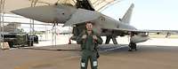 Ein Soldat in Fliegerkombi posiert lächelnd vor einem Eurofighter für ein Foto.