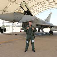Ein Soldat in Fliegerkombi posiert lächelnd vor einem Eurofighter für ein Foto.
