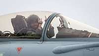 A man sits in a cockpit and poses towards the camera.
