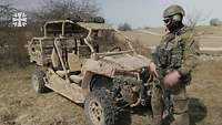 Ein Soldat steht auf einem offenen Gelände vor einem Utility Terrain Vehicle (UTV)