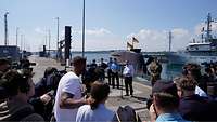 Der Bundesminister steht an einer Pier vor mehreren Personen.