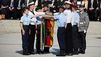 Soldaten stehen auf dem Paradeplatz und legen ihre Hand über die Truppenfahne 