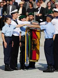 Soldaten stehen auf dem Paradeplatz und legen ihre Hand über die Truppenfahne 