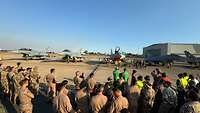 Soldiers stand on an airfield and look towards several stationary fighter jets.