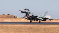 A fighter jet lands on an airfield.