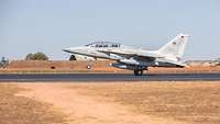 A fighter jet lands on an airfield.