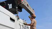 Ein Soldat gibt ein Handzeichen zum Bediener eines Containerstaplers