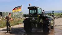 Ein Soldat spritzt einen Gabelstapler Merlo ab, im Hintergrund weht die Bundesdienstflagge