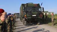 Soldaten stehen Spalier und grüßen militärisch, während Lkw an ihnen vorbeifahren