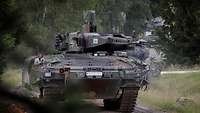 Vier Schützenpanzer fahren hintereinander auf einem Waldweg entlang.