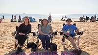 Am Strand sitzen drei Personen mit dem Meer im Hintergrund