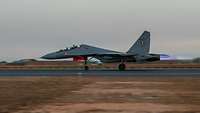 A fighter jet takes off from an airfield at dawn.